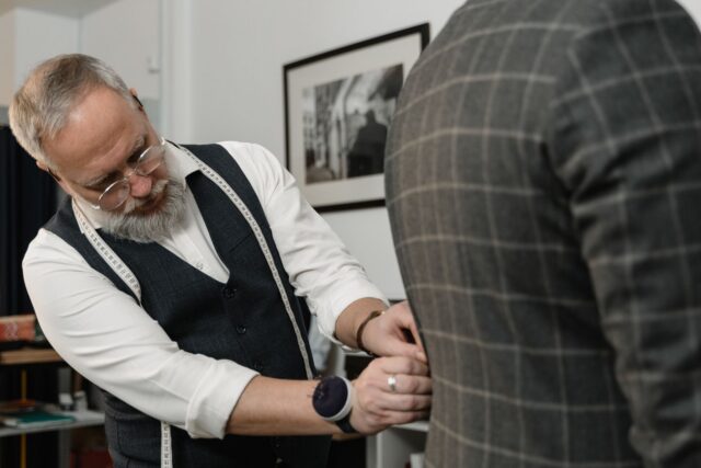 Croitor care ajustează mâneca unui sacou bărbătesc în timpul probei, într-un atelier luminos